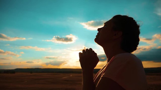 girl praying. girl folded her hands in prayer silhouette at sunset. slow motion video. Girl folded her hands lifestyle in prayer pray to God. asks forgiveness for sins of repentance. believing girl