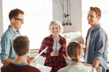 Team  of creative business professionals discussing ideas while collaborating during meeting in modern office or cafe, focus on blonde young woman smiling cheerfully
