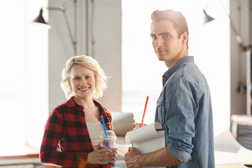 Portrait of two young business people wearing casual clothes smiling happily looking at camera while working in modern office, focus on handsome man in front, copy space