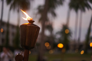 Traditional torches are lit at sunset along the beach, against the backdrop of night lights and a...