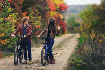 Fototapeta premium curly-haired mustachioed guy and an ore-haired girl in autumn stand with bicycles on road and show cheerful emotions.