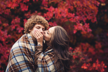 happy couple is hiding behind plaid autumn day against background of red trees.