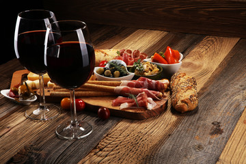 Italian antipasti wine snacks set. Cheese variety, Mediterranean olives, crudo, Prosciutto di Parma, salami and wine in glasses over wooden grunge background.