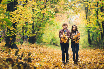 Loving happy couple in autumn in park holding autumn maple leaves in hands.