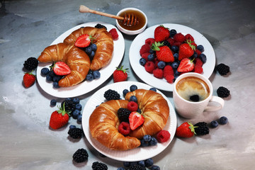 Delicious breakfast with fresh croissants and ripe berries on old marble background.