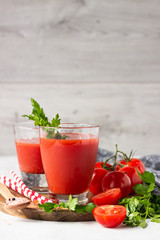 Tomato juice with fresh tomatoes, parsley, sea salt and pepper on light grey background. Vegetable drink.