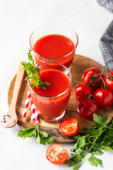 Tomato juice with fresh tomatoes, parsley, sea salt and pepper on light grey background. Vegetable drink.