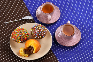 Baking with tea and chocolate on the table.  Two cups of tea with cupcakes and chocolate with a multicolored powder on the table.