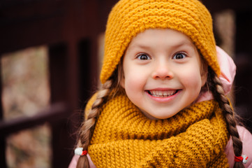 autumn close up portrait of happy little child girl enjoying the walk in sunny park in warm knitted hat and scarf