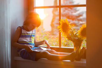 Cute little toddler child, playing on tablet on a window
