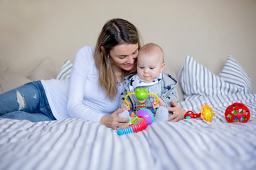 Cute little baby boy, playing with his mom at home in bed with lots of colorful toys