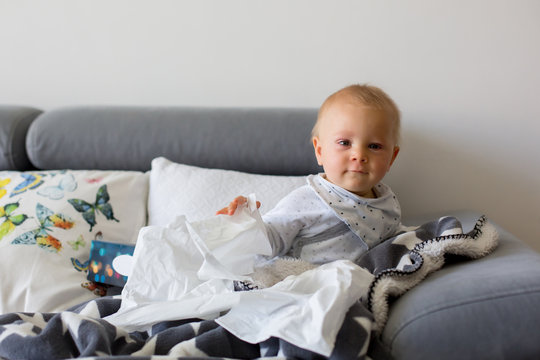 Sick little toddler boy, sitting on a couch in living room