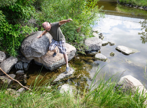 Caucasian Male Stepping Carefully Over Big Rocks By The Lake