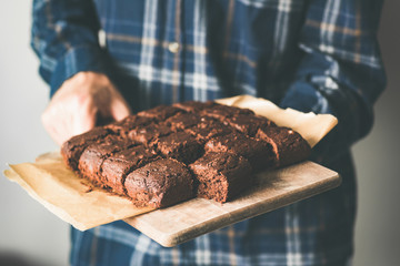 Vegan chocolate brownies on baking sheet. Young person holding plate with freshly baked vegan...