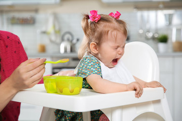 Mother feeding her little baby with healthy food in kitchen
