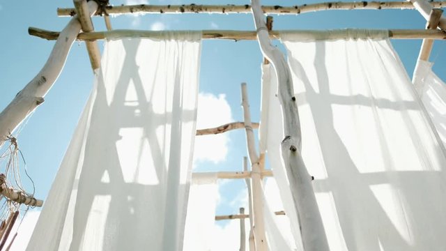 White linen cloth on wooden poles swings in the wind. Against the blue sky and green trees and fields.