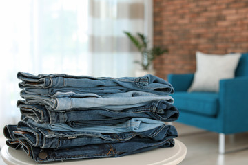 Stack of stylish jeans on table against blurred background