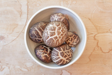 Small bowl of dried shiitake mushroom caps centered on a weathered wood background, horizontal aspect
