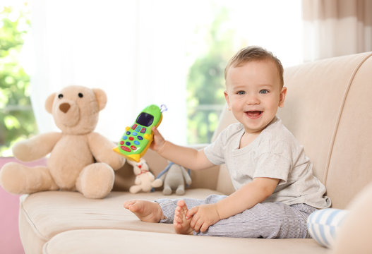 Adorable little baby with toy phone on sofa at home