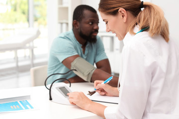 Young doctor checking African-American patient's blood pressure in hospital