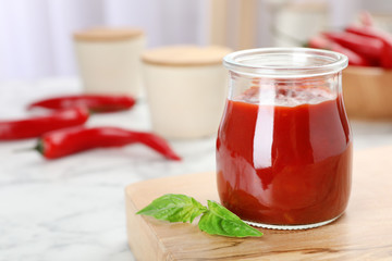 Jar with spicy chili sauce on marble table