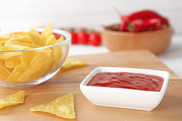 Bowl with spicy chili sauce and chips on table