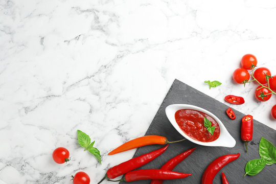 Flat lay composition with gravy boat of spicy chili sauce on marble background