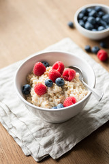 Bowl of oatmeal porridge with berries on textile on wooden table. Selective focus. Healthy breakfast, healthy eating concept