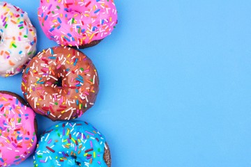 Side border of assorted donuts with frosting and sprinkles against a pastel blue background