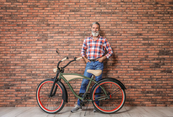 Fototapeta premium Portrait of handsome mature man with bicycle near brick wall