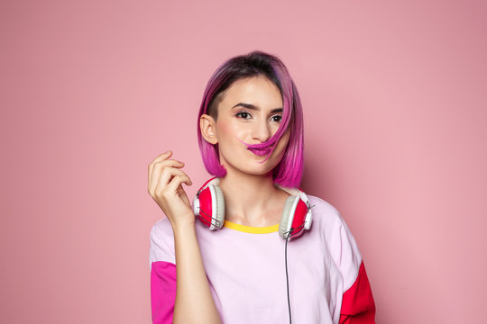 Young woman with trendy hairstyle and headphones against color background