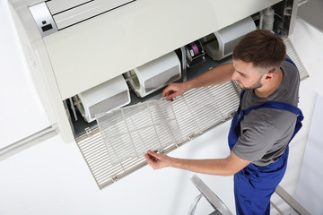 Young male technician cleaning air conditioner indoors