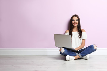 Naklejka premium Young woman with modern laptop sitting near color wall