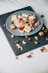 Traditional oriental sweets and nuts: hazelnuts, cashews on a white wooden background. Turkish dessert is the locus of Rahat. View from above. Place under the text.