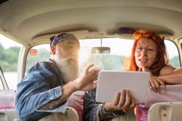 A senior hipster couple sitting in a van, using a digital tablet