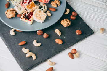 Traditional oriental sweets and nuts: hazelnuts, cashews on a white wooden background. Turkish dessert is the locus of Rahat. View from above. Place under the text.