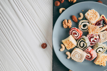 Traditional oriental sweets and nuts: hazelnuts, cashews on a white wooden background. Turkish dessert is the locus of Rahat. View from above. Place under the text.