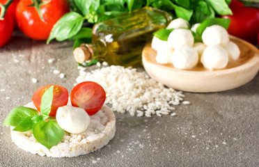 Small balls of mozzarella with basil leaves and tomato on rice bread on rustic background