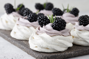 Pavlova dessert cakes with soft lavender cream and fresh blackberries decorated with rosemary...