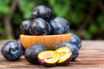 Fresh ripe plums and halves in wooden bowl close