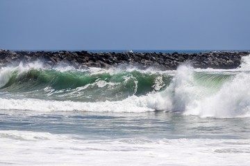 waves crashing on the shore with a rock jetty in the background 