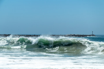 Fototapeta premium waves crashing on the shore with a rock jetty in the background 