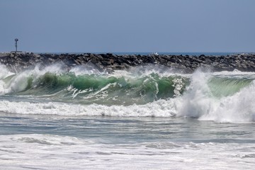 waves crashing on the shore with a rock jetty in the background 