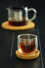 modern glass tea cup with cork saucer and teapot over black dining table - vertical