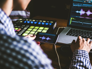close up person creating music using phone and other sound equipment with laptop
