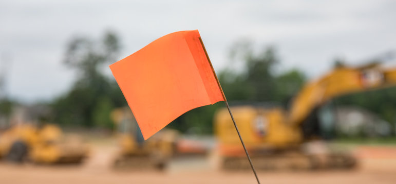 A bokeh close up shot of a warning flag at a construction site with heavy machinery equipment in the background.