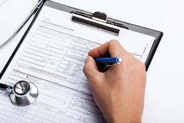 Hand Filling a Health Insurance Document with Stethoscope