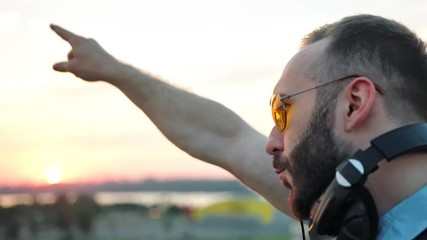 Profile of fashionable DJ with headphones and sunglasses enjoying music at summer rooftop party