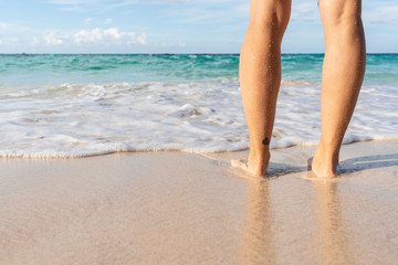 Young woman legs and feet standing on beach