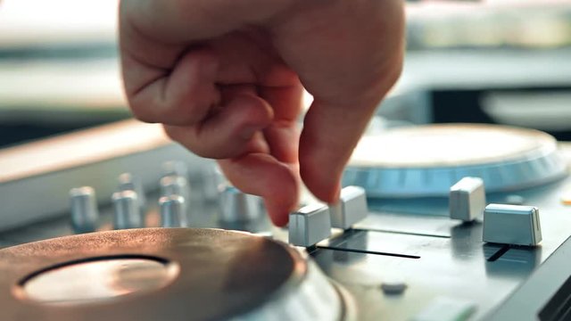 Male hands of Disk Jockey mixing music tracks tweak various controls on deck